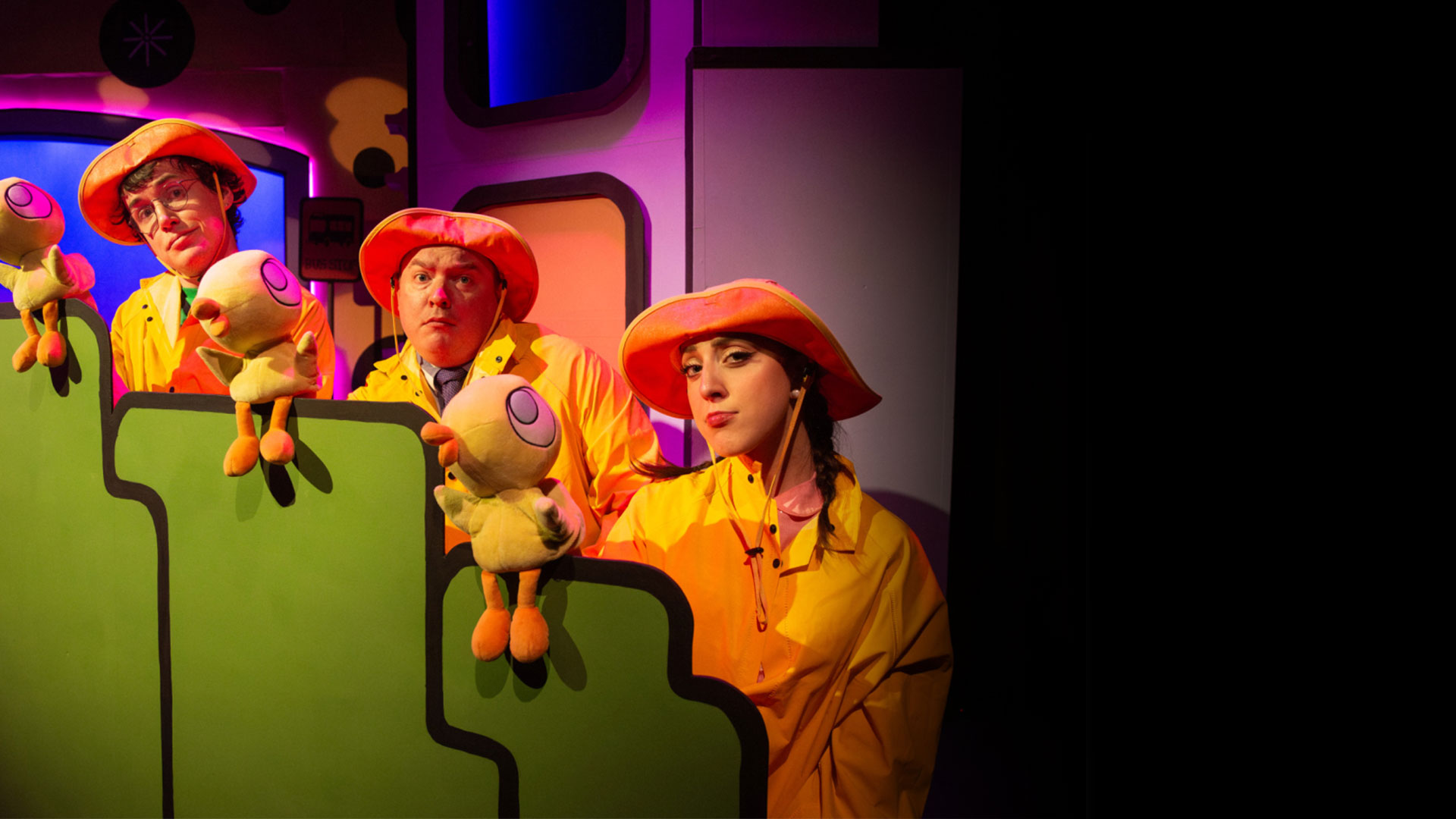 Three people dressed in yellow raincoats with duck puppets on their hands